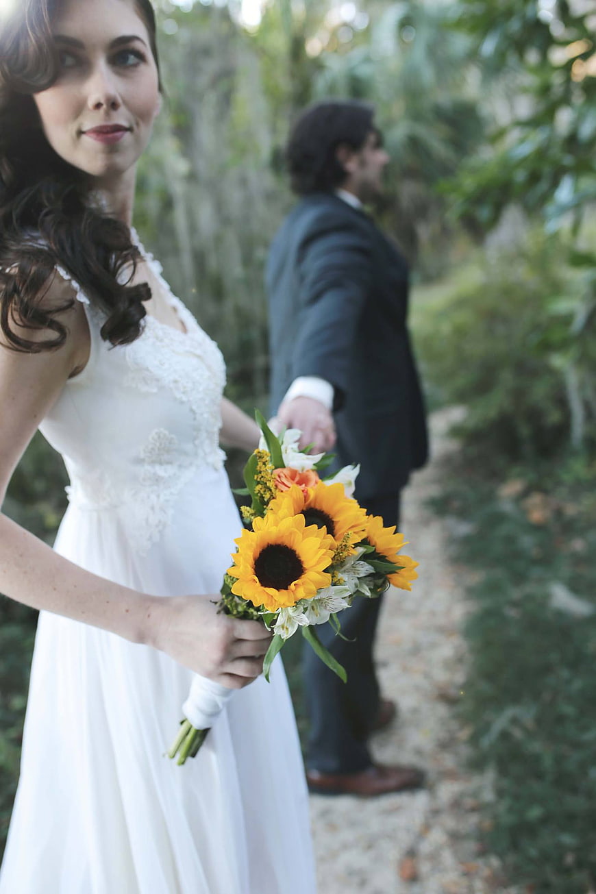 Bride with Sunflower Bouquet and Groom in Background