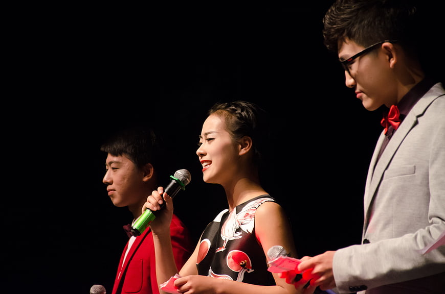 Three young hosts presenting on stage with microphones