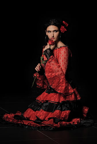 Woman in red lace dress holding rose against black background