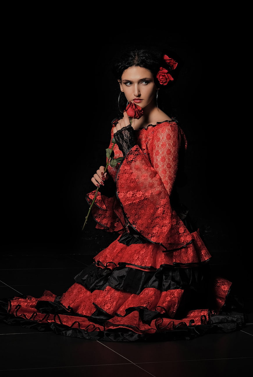 Woman in red lace dress holding rose against black background