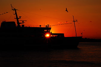 Silhouette of Ferry Boat Against Vibrant Orange Sunset Sky
