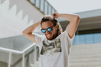 Happy man with dreadlocks and sunglasses fixing hair outdoors