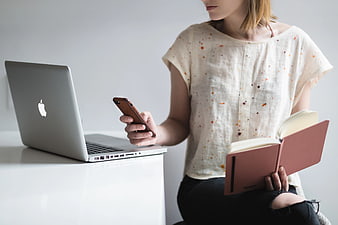 Woman with Smartphone, Book, and Laptop at Desk