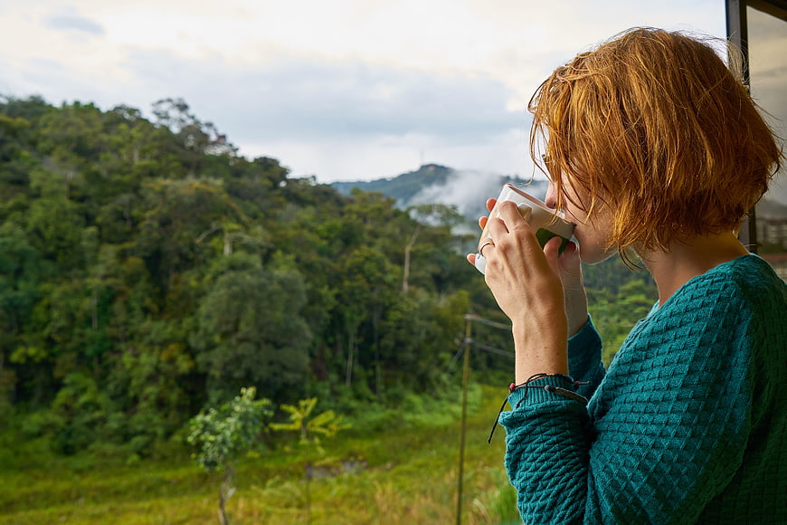 Woman drinking coffee on balcony overlooking lush green mountains
