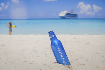 Blue beer bottle buried in white sand beach with cruise ship background