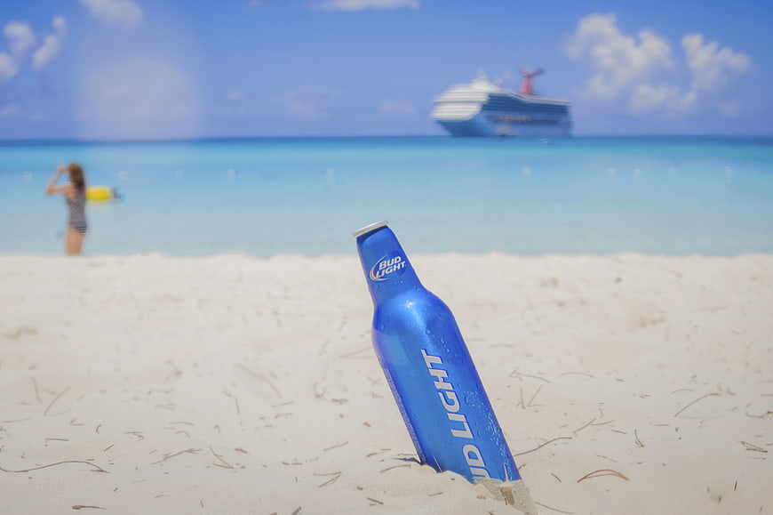 Blue beer bottle buried in white sand beach with cruise ship background