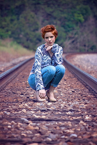 Redhead woman squatting on railroad tracks outdoors