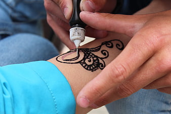 Close-up of hands applying black henna tattoo design on forearm