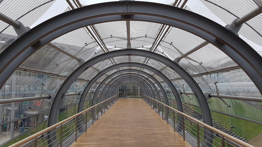 Modern arched metal walkway with wooden floor and mesh roof