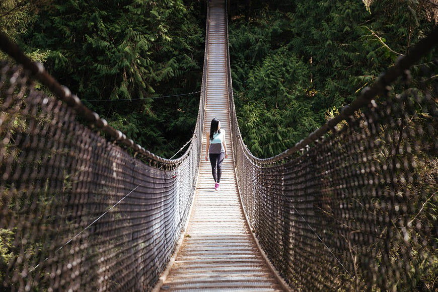 Woman Walking on Suspension Bridge in Forest