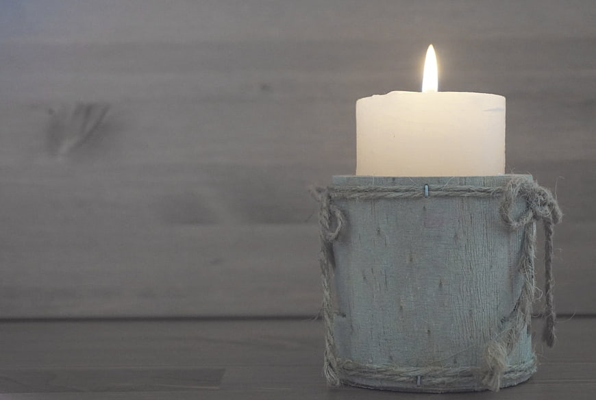Lit white candle in rustic wooden holder with twine