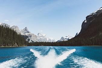 Boat wake on turquoise lake with snow-capped mountains