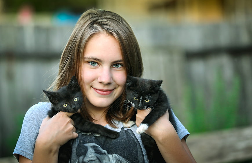 Teenage girl holding two black kittens outdoors