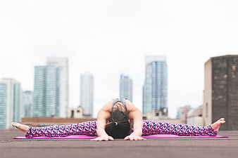 Woman doing splits yoga pose on rooftop with city skyline