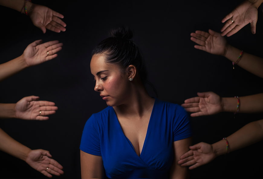 Woman surrounded by reaching hands on black background