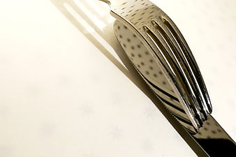Close-up of shiny silver fork and knife on white tablecloth