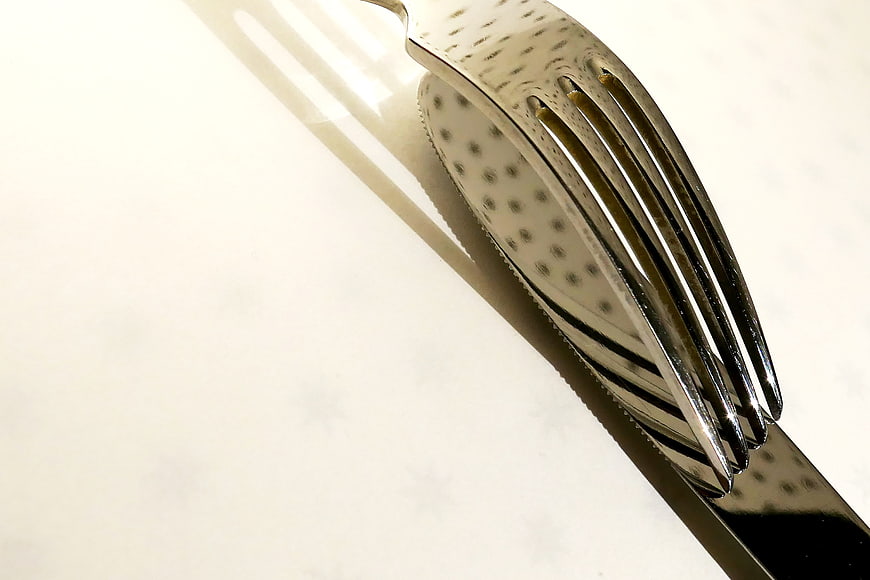 Close-up of shiny silver fork and knife on white tablecloth