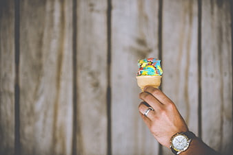 Hand holding colorful rainbow ice cream cone against wooden background