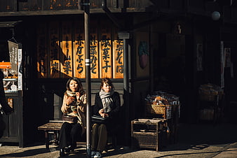 Two women resting on a bench in front of a traditional Japanese shop