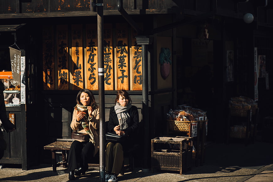 Two women resting on a bench in front of a traditional Japanese shop