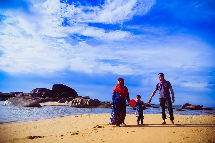 Family Walking on Sandy Beach with Blue Sky and Rocks
