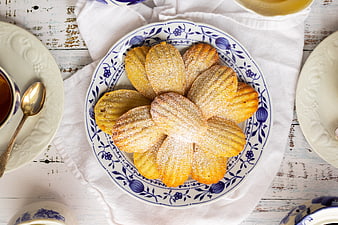 Top view of powdered sugar madeleine cookies on blue floral plate