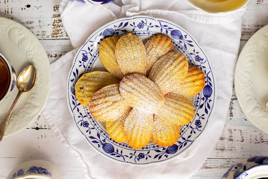 Top view of powdered sugar madeleine cookies on blue floral plate