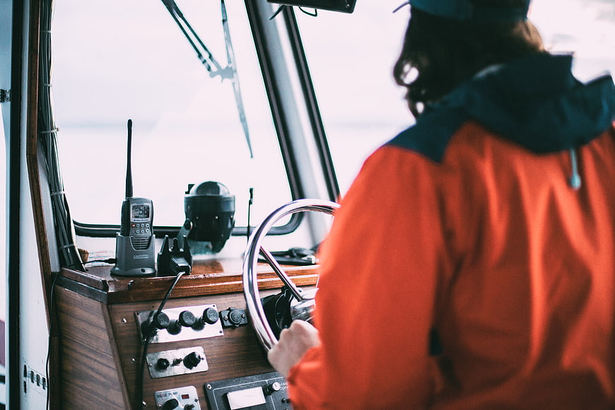 Sailor steering boat wheel in cabin with radio