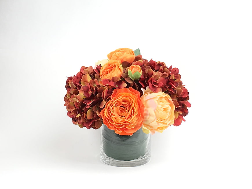 Autumn floral arrangement with orange roses and red hydrangeas in a glass vase