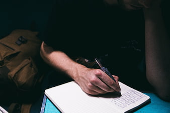 Man Writing in Notebook with Pen in Dark Room