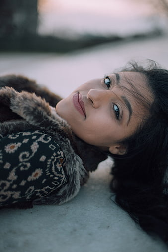 Woman lying in snow wearing fur coat and patterned sweater