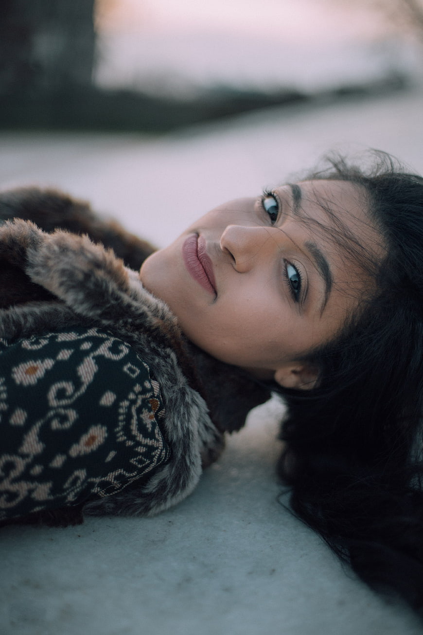 Woman lying in snow wearing fur coat and patterned sweater