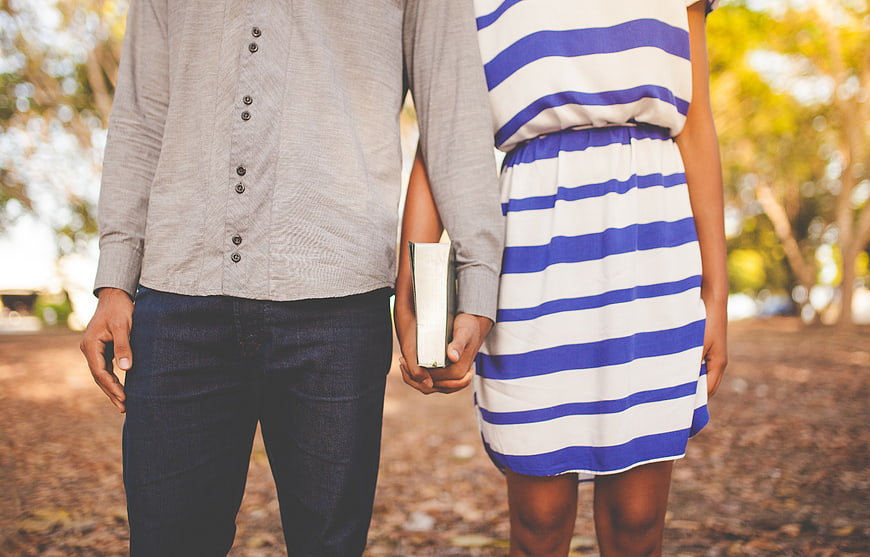 Couple holding hands and a book outdoors in a park
