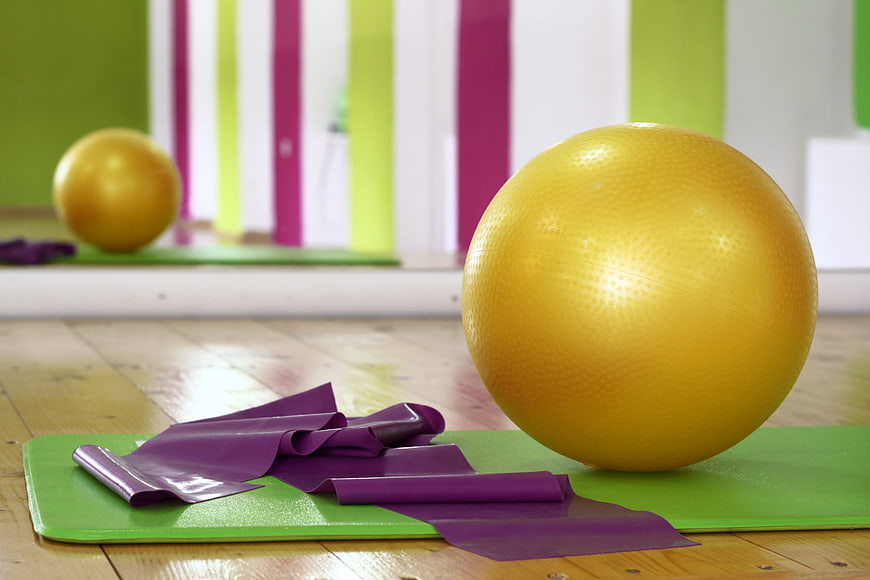 Yellow exercise ball and purple resistance bands on green yoga mat