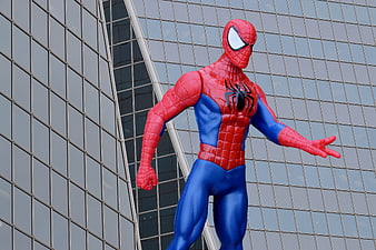Spider-Man statue standing in front of modern glass skyscraper