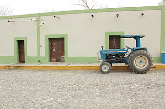 Blue Tractor Parked on Cobblestone Street in Rural Town