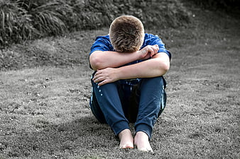 Sad young boy sitting alone on grass with head down