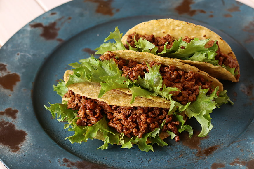 Three beef tacos with lettuce on a rustic blue plate