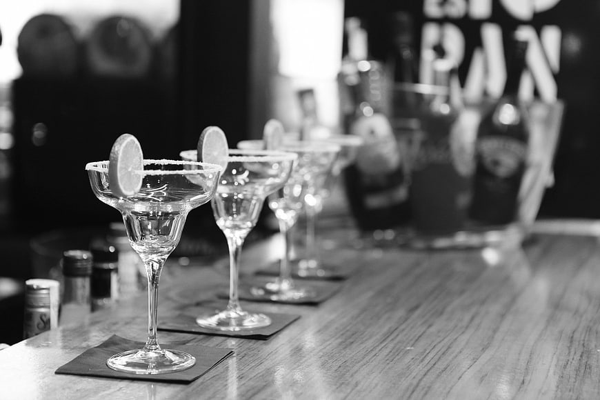 Black and white margarita glasses lined up on a bar counter
