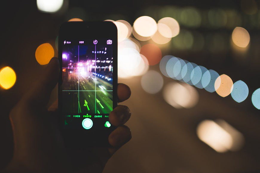 Hand holding smartphone taking photo of city bokeh at night