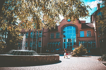 Woman walking past historic brick building with fountain