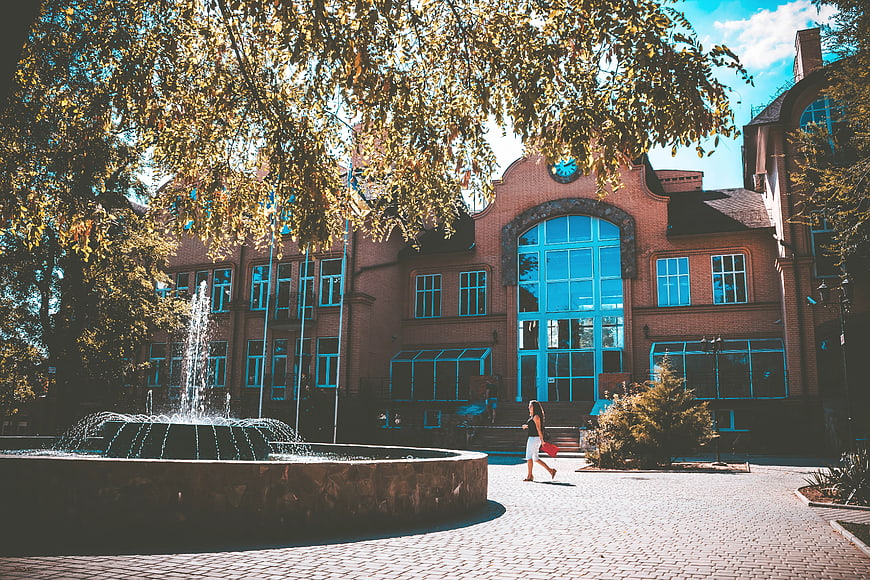Woman walking past historic brick building with fountain