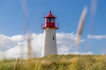 Red and white lighthouse on grassy dune against blue sky