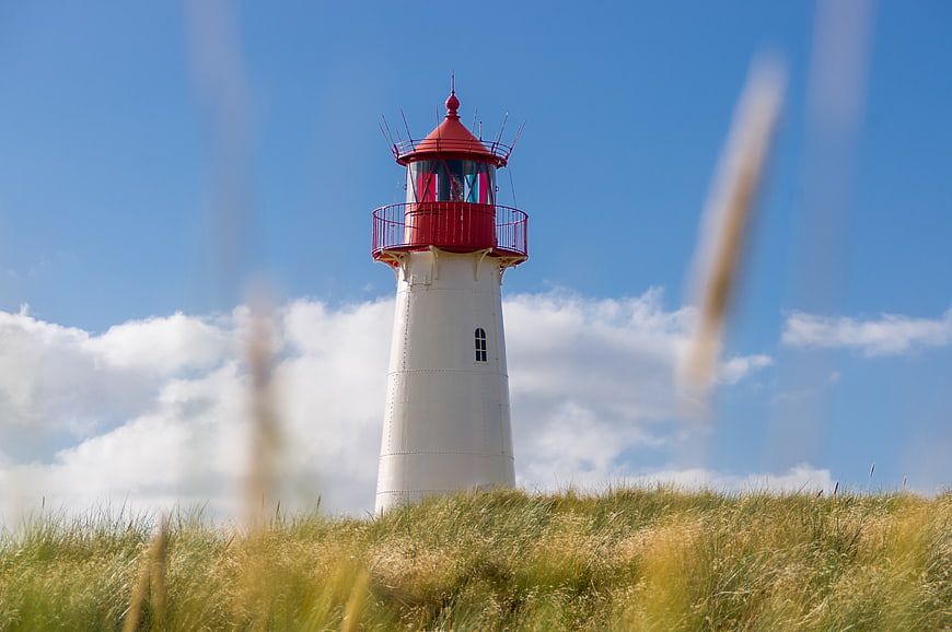 Red and white lighthouse on grassy dune against blue sky