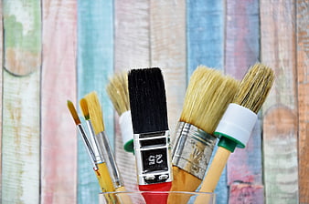 Assorted Paint Brushes In Glass Jar Against Pastel Wooden Background