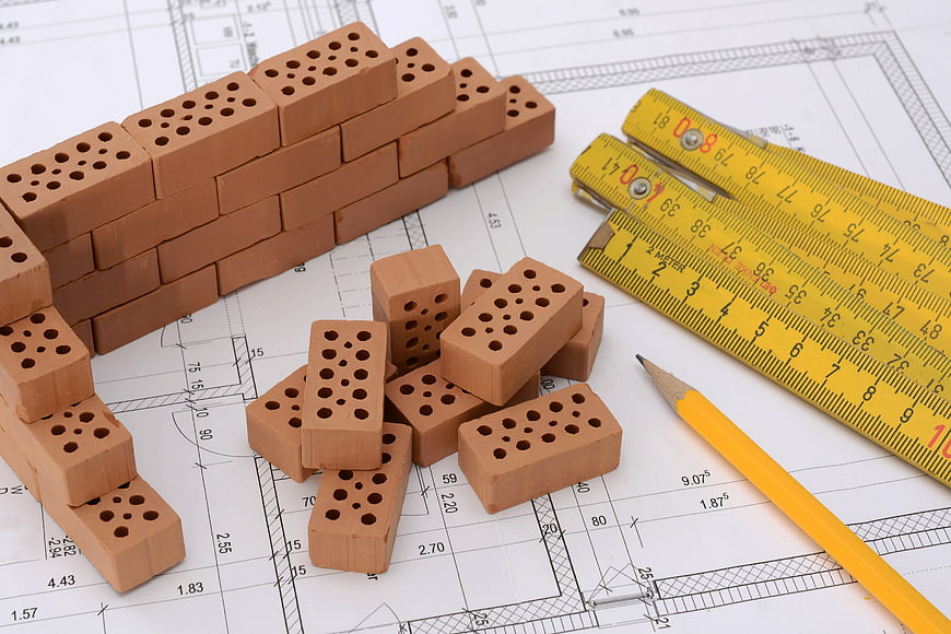 Miniature bricks, yellow tape measures, and pencil on architectural blueprint