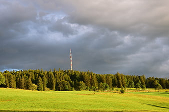 Dramatic storm clouds over green meadow and forest with antenna