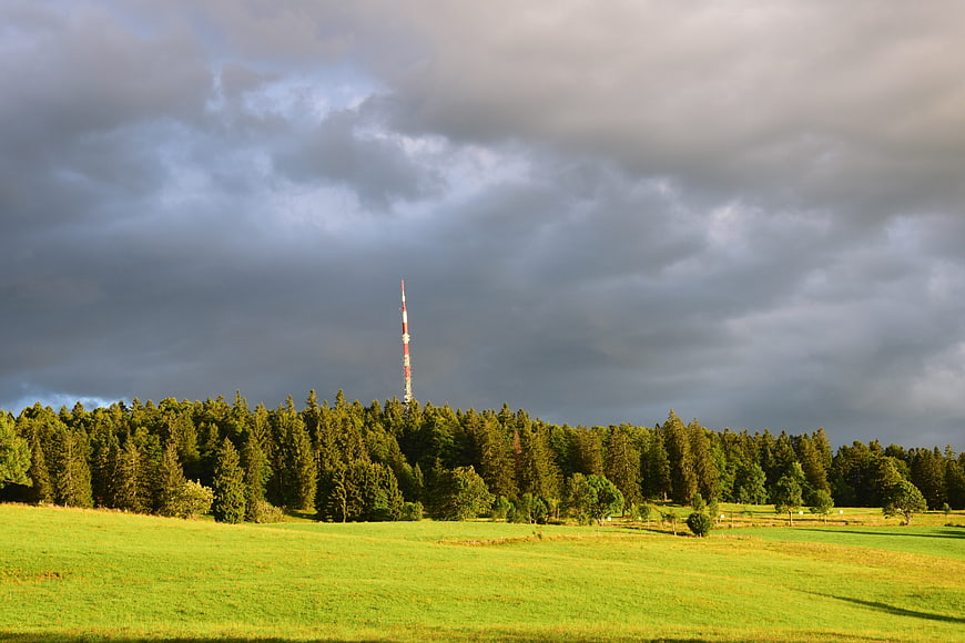 Dramatic storm clouds over green meadow and forest with antenna