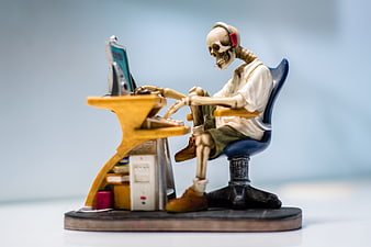 Skeleton figure wearing headphones typing on a miniature computer desk