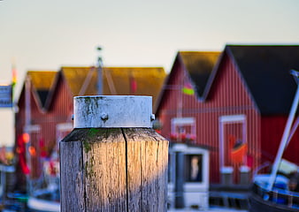 Weathered wooden bollard with blurred red harbor buildings in background